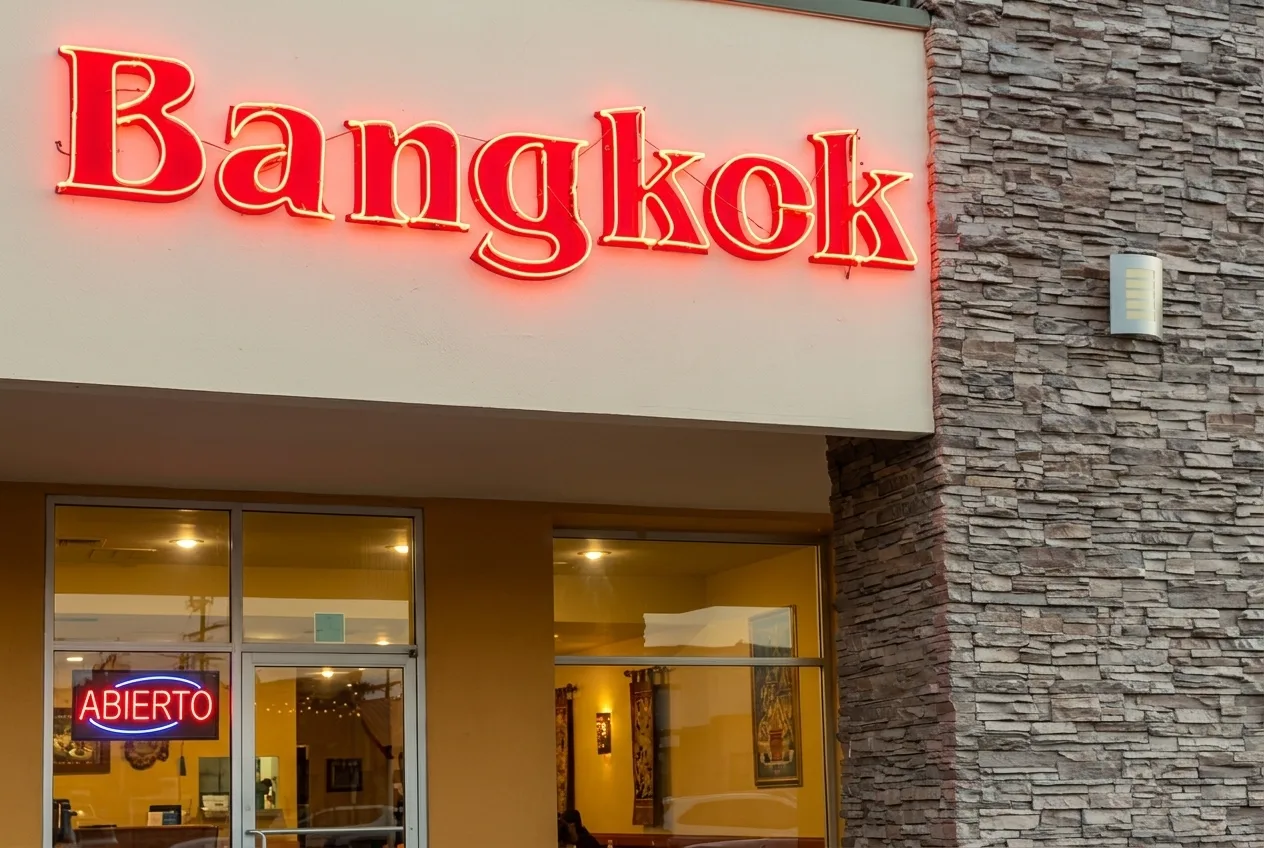 Fachada de Bangkok Cocina Tailandesa en Plaza Cataviña: letrero de neón rojo «Bangkok», ventanales con luz cálida y columna de piedra